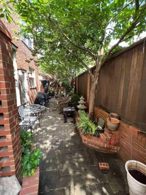 Lush backyard with mature trees, garden decor, and outdoor seating on a paved patio.